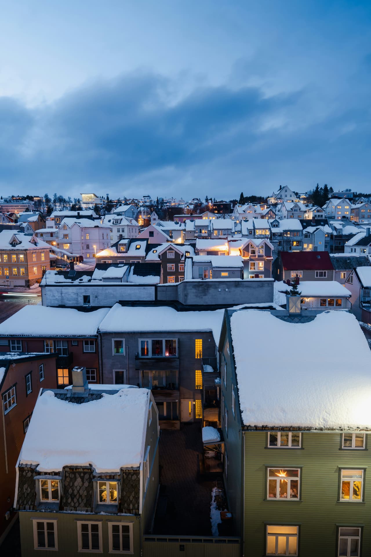 Snötäckta tak och varmt ljus i fönster en vinterkväll