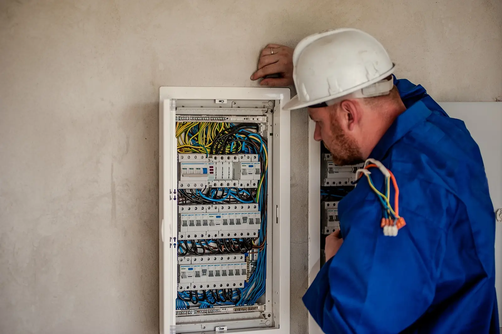 Elektriker i blå arbetskläder kopplar i en elcentral