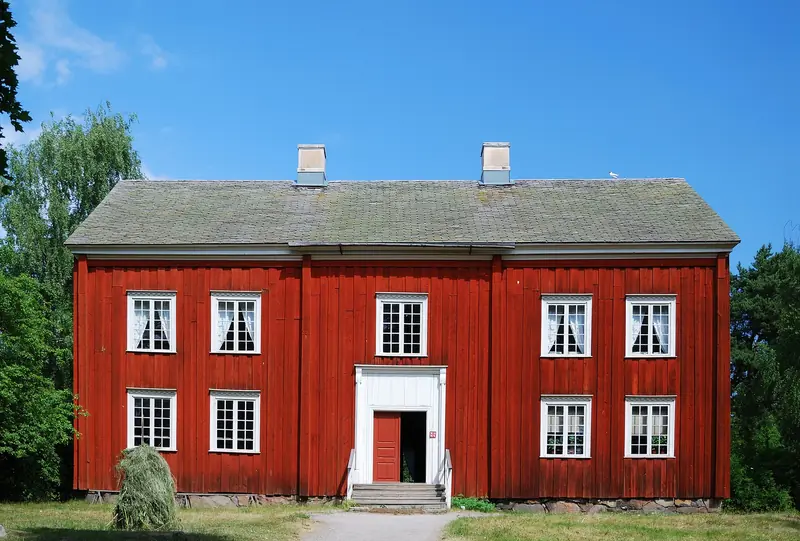 Stort rött trähus i två våningar med vita knutar och blå himmel